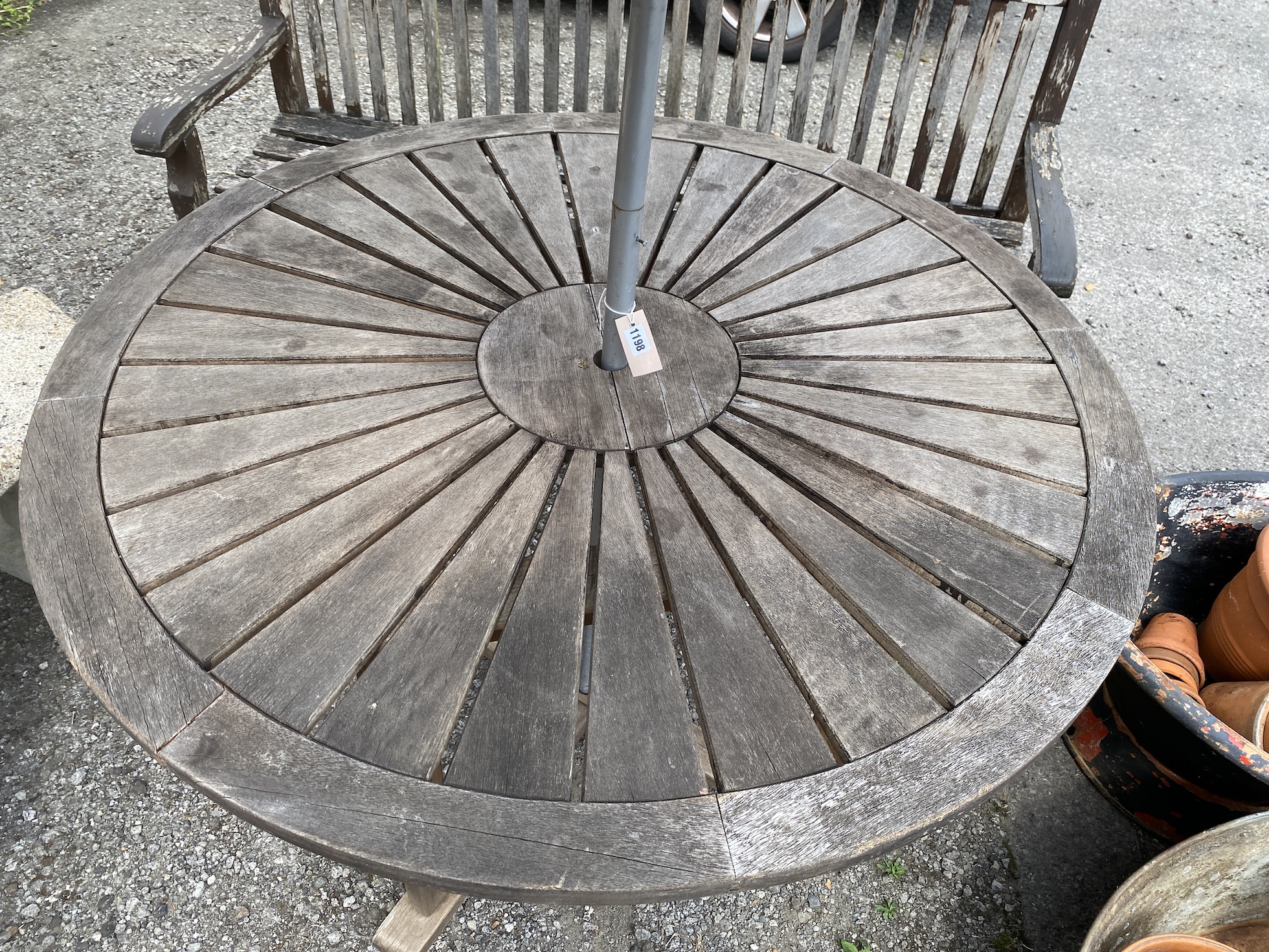 A circular weathered teak garden table, diameter 122cm, height 75cm parasol and bench